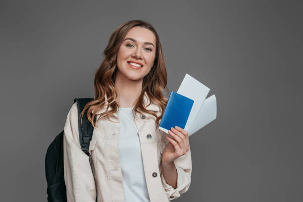 study abroad concept. student girl holding backpack, book, notebook, passport isolated on a dark grey background, copy space, immigration,